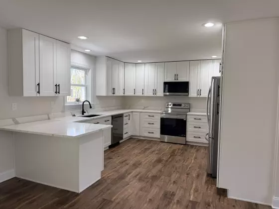 Remodeled open-concept kitchen in Locust Grove, VA with white shaker cabinets, quartz peninsula, and stainless steel appliances