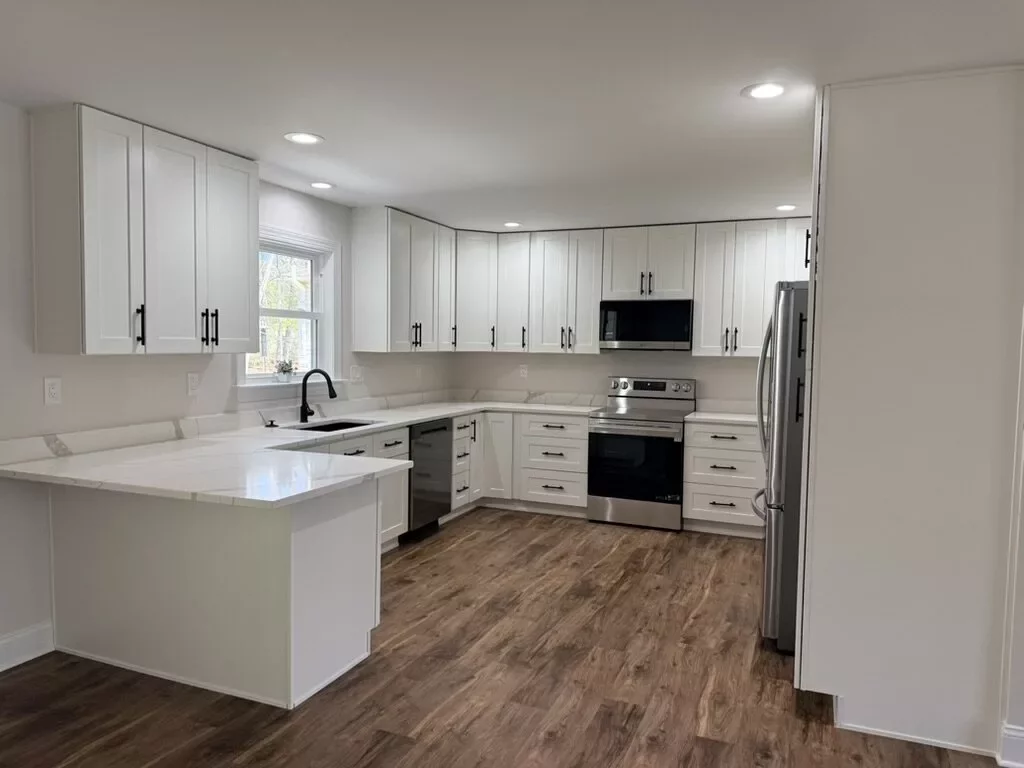 U-shaped white kitchen with quartz counters, black faucet, stainless appliances, and a window above the sink