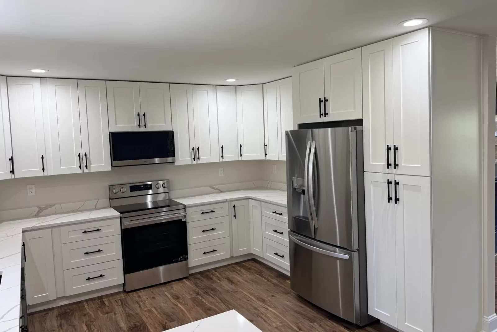 White shaker kitchen with stainless steel range, French-door refrigerator, quartz countertops, and wood-look flooring