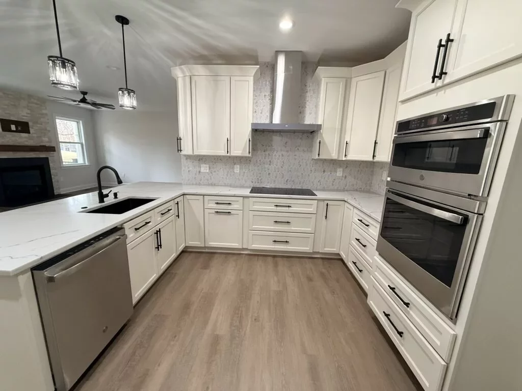 White shaker kitchen with a tile backsplash, built-in cooktop, double wall ovens, and quartz countertops