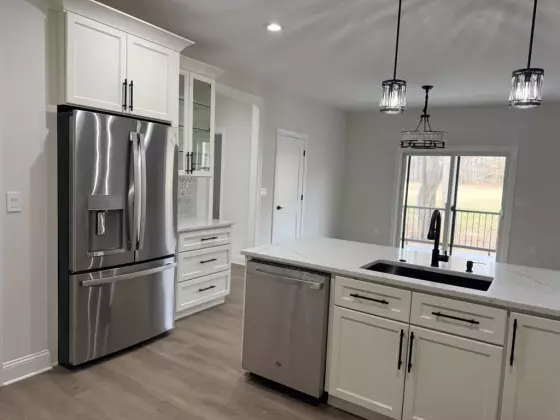 Open-concept kitchen with white cabinets and quartz island opening into the living and dining area