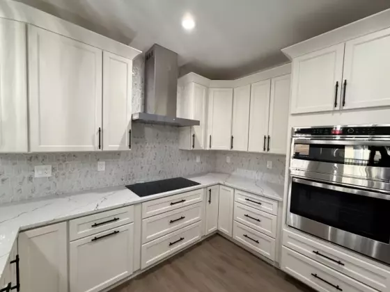 U-shaped custom kitchen with white cabinetry, range hood, quartz counters, and wood-look flooring