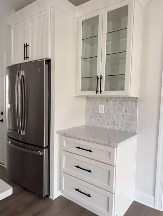 Stainless steel French-door refrigerator framed by white cabinetry with glass-front upper cabinets
