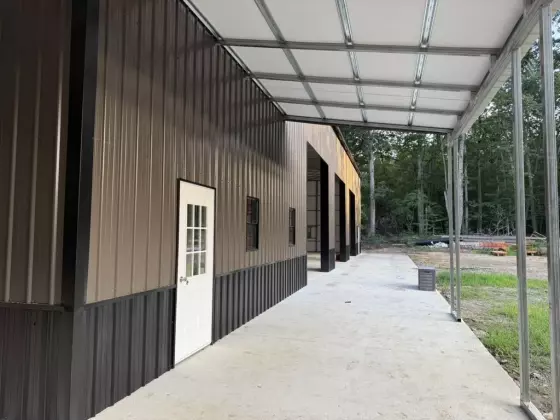 Covered side walkway of the finished metal building with concrete path, white entry door, and dark steel siding