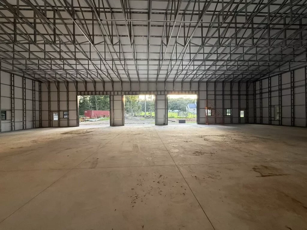 Wide-span interior of the metal building with steel framing and two large open bay doors at the far end