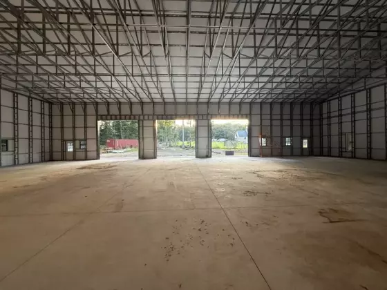 Wide-span interior of the metal building with steel framing and two large open bay doors at the far end
